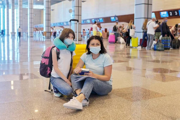 Madre e hija niño en máscaras médicas protectoras en el aeropuerto con equipaje —  Fotos de Stock