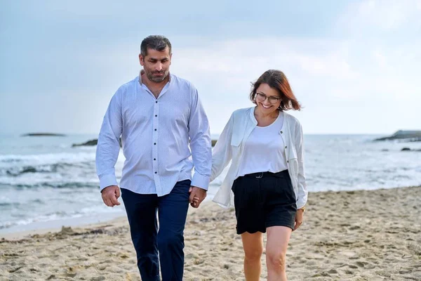 Kumsalda birlikte yürüyen mutlu orta yaşlı çift..