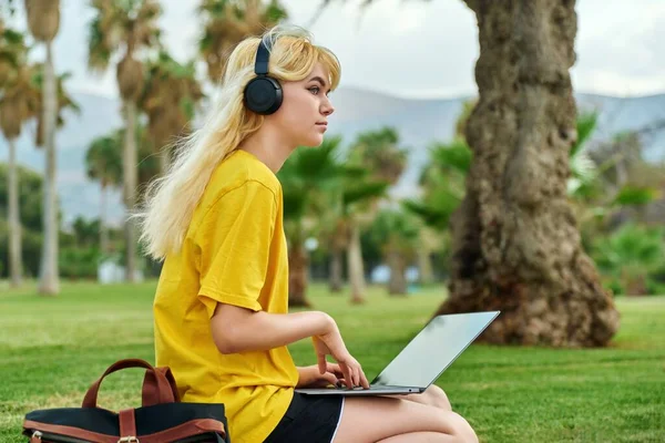 Жінка-підліток у навушниках сидить у парку з ноутбуком . — стокове фото