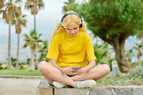 Hermosa adolescente en auriculares con teléfono inteligente al aire libre. — Foto de Stock