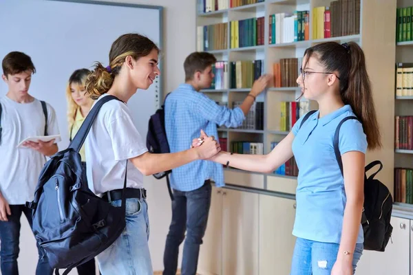 Amigos adolescentes los estudiantes se abrazan cuando se encuentran en la biblioteca — Foto de Stock