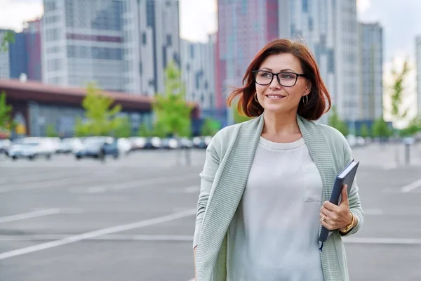 Sorrindo bem sucedido mulher de negócios maduro andando ao ar livre, moderno estilo urbano fundo. — Fotografia de Stock