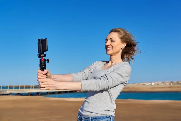 Женщина средних лет записывает видео на смартфон на открытом воздухе на берегу моря — стоковое фото