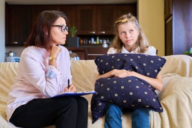 Sosyal hizmetli kadın, kız çocuğuyla konuşuyor, panoya not alıyor..