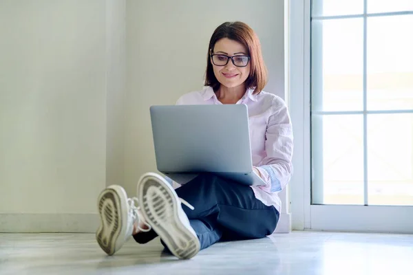 Donna di mezza età seduta sul pavimento utilizzando il computer portatile — Foto Stock