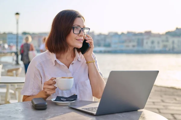 Επιχειρηματίας κάθεται σε υπαίθριο καφέ με φλιτζάνι καφέ χρησιμοποιώντας φορητό υπολογιστή και έξυπνο τηλέφωνο — Φωτογραφία Αρχείου