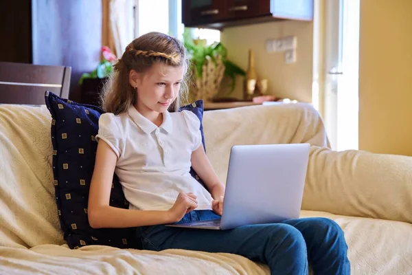 Bambino ragazza a casa sul divano con un computer portatile. — Foto Stock