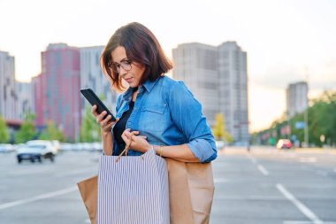 Şehirde akıllı telefon kullanan orta yaşlı bir kadın.