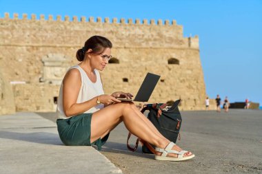 Laptop kullanan olgun bir kadın turist, eski Avrupa tarihi kalesi geçmişi.