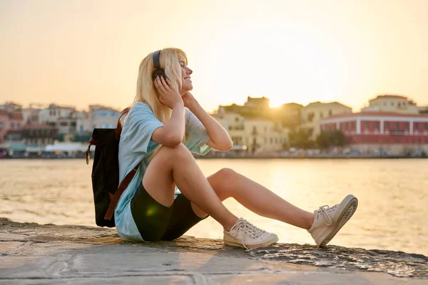 Feliz adolescente turista sentada en el paseo marítimo de una ciudad vieja al atardecer — Foto de Stock