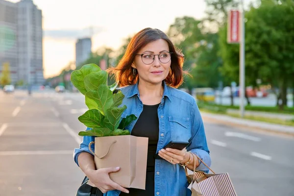 Mulher com sacos de papel de compras, planta comprada andando ao ar livre — Fotografia de Stock