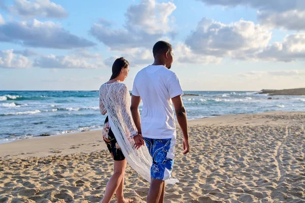 Fiatal boldog pár sétál a parton kéz a kézben, visszapillantás. — Stock Fotó