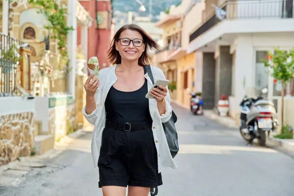 여름 도시의 거리를 걷고 있는 아이스크림을 먹는 여성 — 스톡 사진