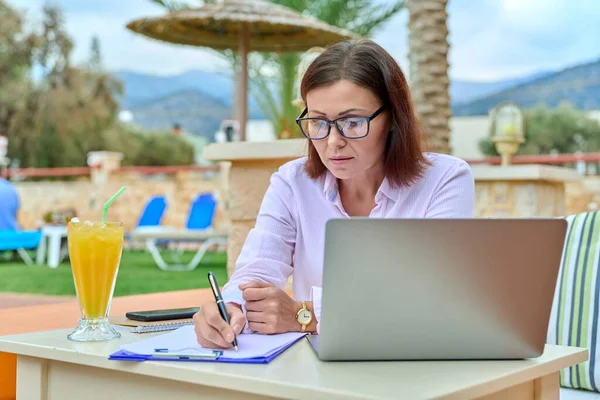 Ώριμη γυναίκα των επιχειρήσεων που εργάζονται με φορητό υπολογιστή, κάθεται έξω κοντά στην πισίνα — Φωτογραφία Αρχείου