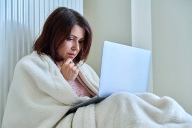 Kadın ısıtma radyatörüyle ısınıyor, dizüstü bilgisayar kullanıyor..