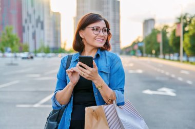 Şehirde akıllı telefon kullanan orta yaşlı bir kadın.