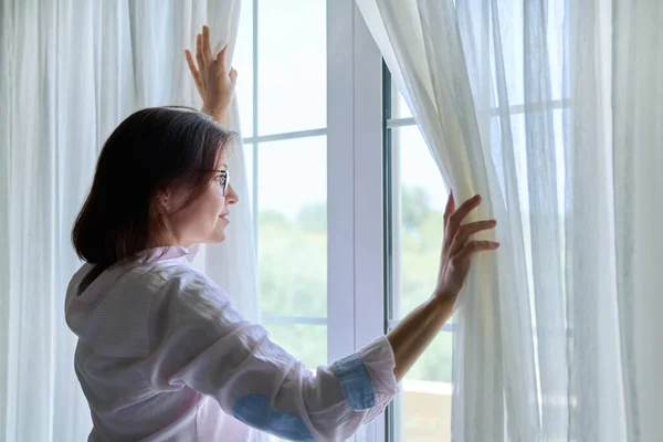 Улыбающаяся зрелая женщина смотрит в окно — стоковое фото