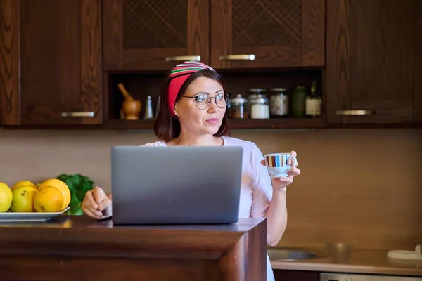 Medelålders kvinna i hemmet kök avkopplande med laptop för fritid och underhållning — Stockfoto