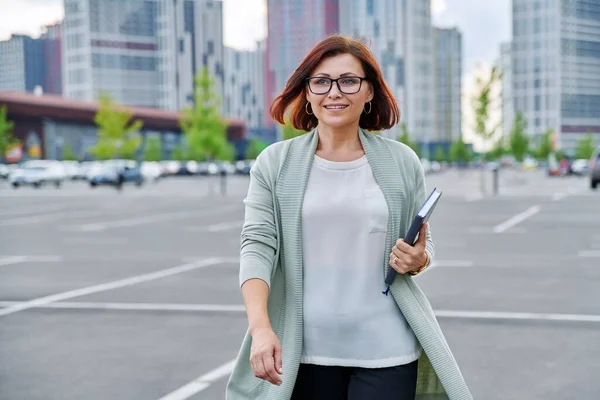 Sorrindo bem sucedido mulher de negócios maduro andando ao ar livre, moderno estilo urbano fundo. — Fotografia de Stock