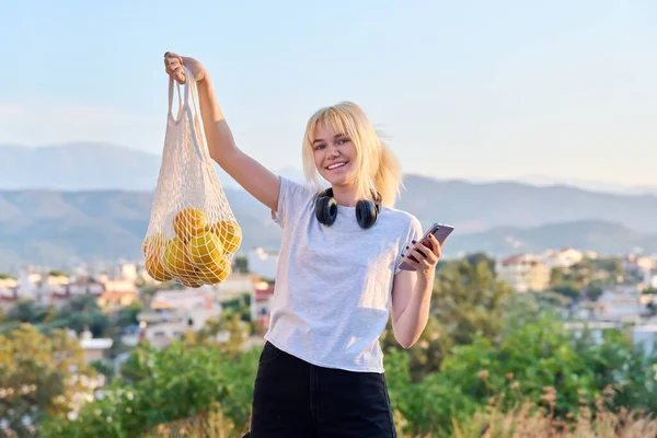 Young teenage woman holding mesh eco bag with fresh organic farm oranges — Stock Photo, Image