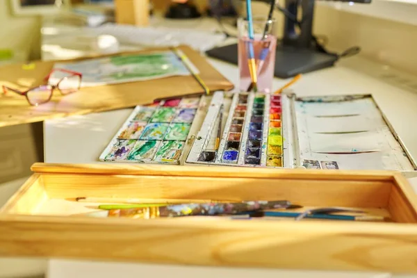 Watercolor drawing, glasses, watercolors in a box, brushes on the table, nobody — Foto Stock