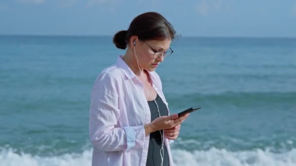 Mujer seria hablando en videollamada usando smartphone con auriculares — Vídeo de stock