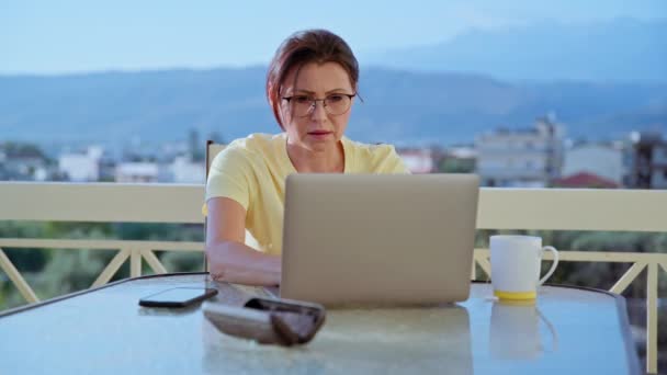 Μεσήλικη γυναίκα που εργάζεται σε ένα γραφείο στο σπίτι σε μια βεράντα. — Αρχείο Βίντεο