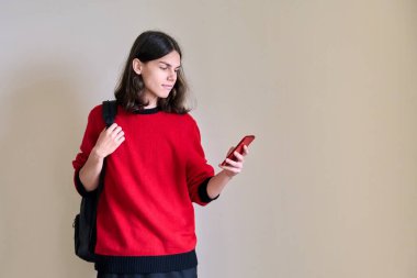 Elinde akıllı telefon olan genç bir erkek, ışık duvarına karşı.