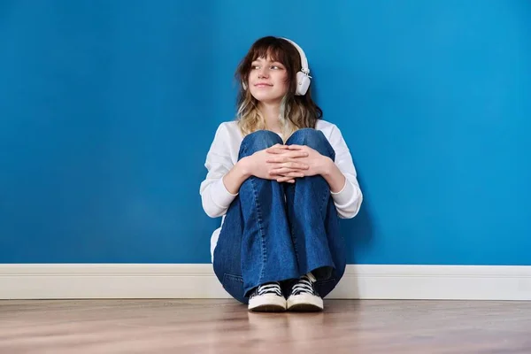Retrato de adolescente em fones de ouvido sentado no chão no fundo azul — Fotografia de Stock