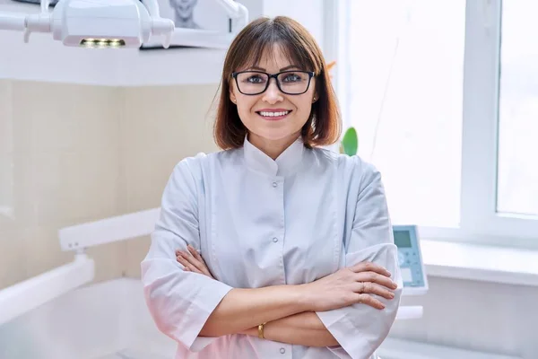 Portret van glimlachende volwassen vrouwelijke tandarts op zoek naar camera in het kantoor — Stockfoto