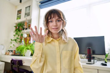 Kablosuz kulaklıklı genç kız öğrenci kameraya bakarak konuşuyor.