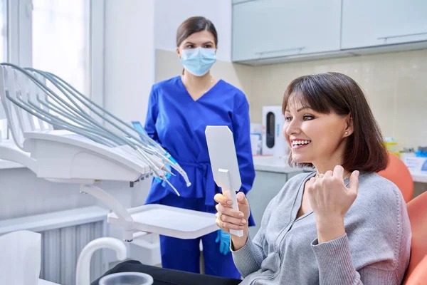 Dentists office, woman patient looking at her teeth in the mirror — Foto de Stock