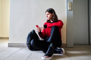 Sırt çantalı, yerde oturan modaya uyan genç bir erkek.