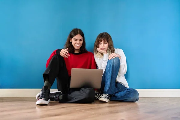 Couple of teenage students using laptop sitting on the floor on blue background — Photo
