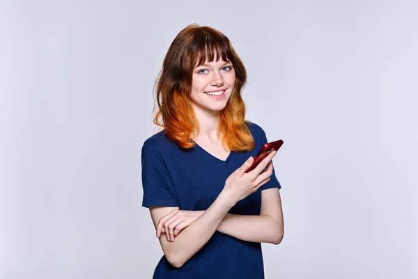 Krásná usměvavá dospívající žena s chytrým telefonem v ruce při pohledu na kameru — Stock fotografie