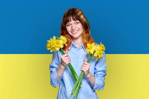 Ukraine flag background, young smiling beautiful woman holding yellow flowers — стоковое фото