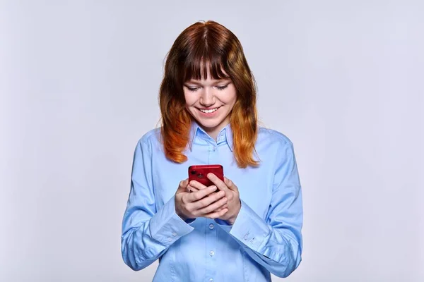Usmívající se dospívající žena při pohledu na obrazovce smartphone, na pozadí světelného studia — Stock fotografie