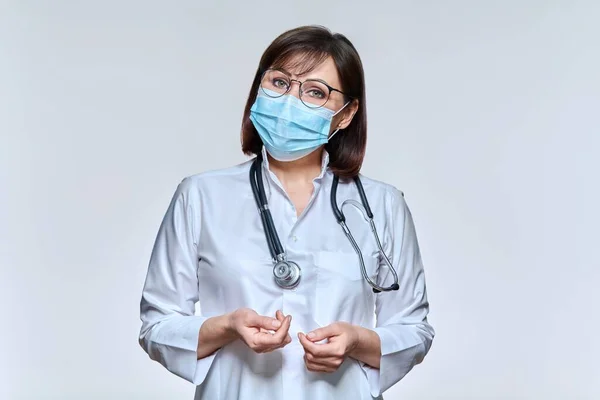 Portrait of female doctor in medical mask looking at camera on light studio background — Stock fotografie