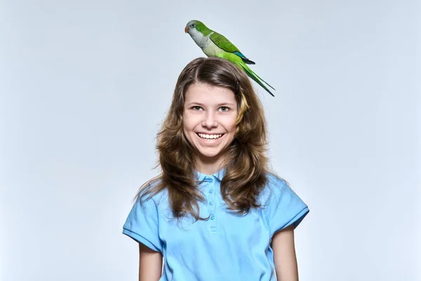 Niña con mascota verde loro cuáquero mirando a la cámara en el fondo del estudio de luz —  Fotos de Stock