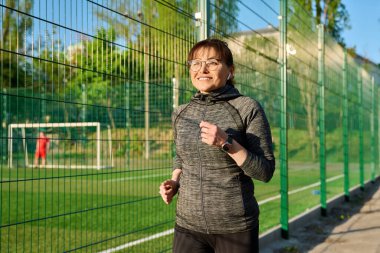 Olgun aktif bir kadın stadyumun yanında koşuyor.