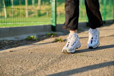 Stadyumun yakınındaki yolda koşan beyaz spor ayakkabılı kadın bacakları.