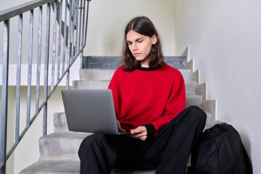 Binadaki basamaklarda dizüstü bilgisayar kullanan öğrenci portresi.