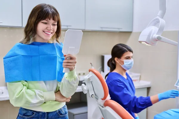 Tiener vrouw op zoek naar gezonde tanden in de spiegel, in tandartspraktijk — Stockfoto