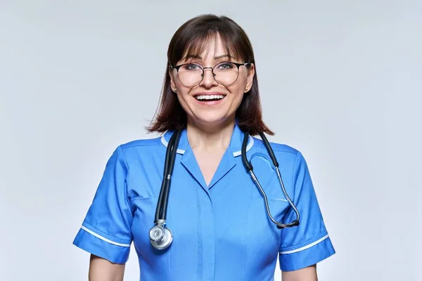 Headshot portrait of nurse in blue uniform looking at camera on light studio background — Fotografia de Stock