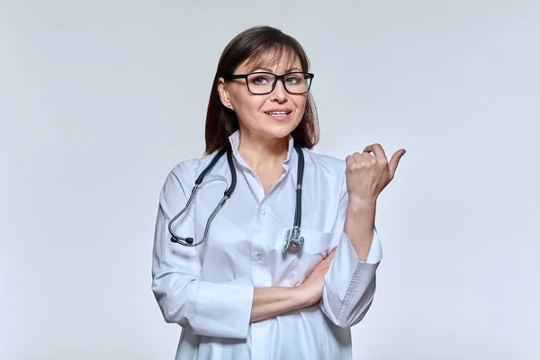 Retrato de médico feminino olhando para câmera falando gestos no fundo do estúdio de luz — Fotografia de Stock