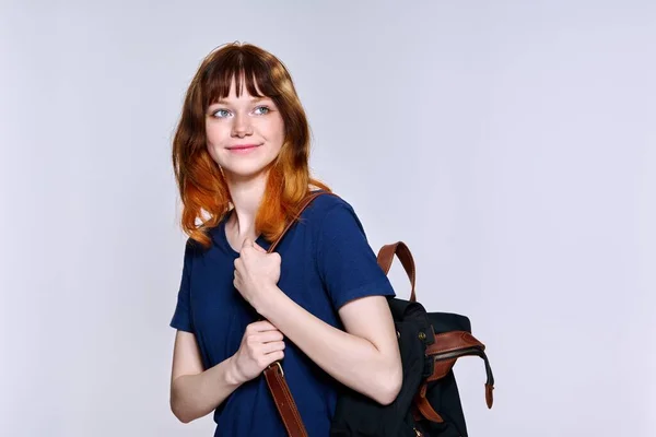 Positive teenage female student with backpack looking away on light studio background — стоковое фото