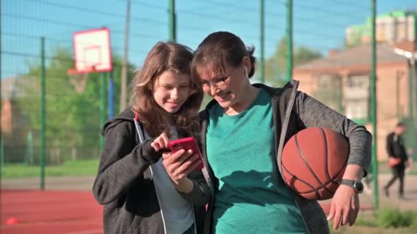 Mamá e hija mirando juntas en la pantalla del teléfono inteligente, al aire libre — Vídeos de Stock