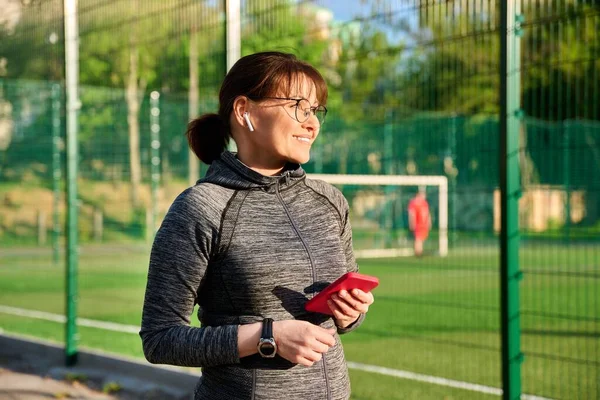 Spor giyim kulaklıklı, akıllı telefonlu, açık havada aktif olgun bir kadın.