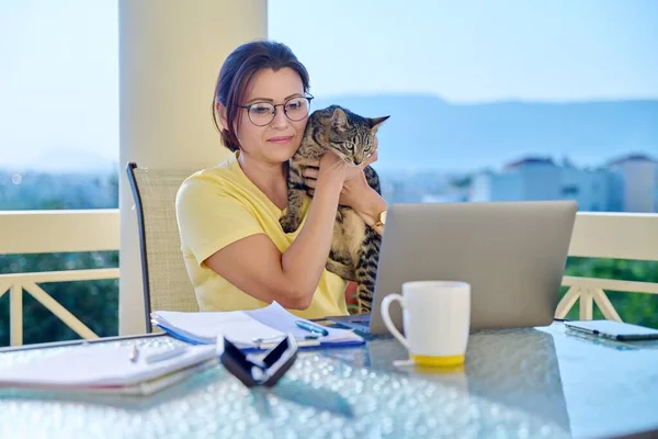 Жінка середнього віку працює вдома з кішкою на руках . — стокове фото