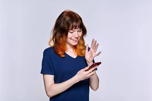 Usmívající se dospívající žena při pohledu na obrazovce smartphone, na pozadí světelného studia — Stock fotografie